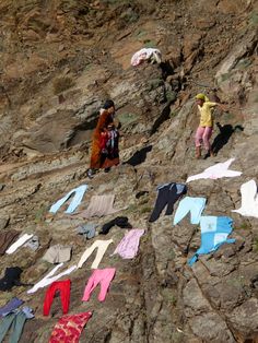 two people standing on the side of a mountain next to clothes