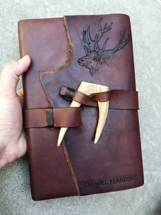 a hand holding a brown leather journal with deer head on it