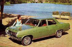 a woman sitting on the hood of a green car next to a body of water