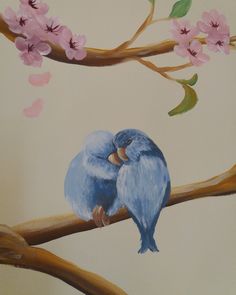 two blue birds are sitting on a branch with pink flowers in the background and one has its face to each other's chest