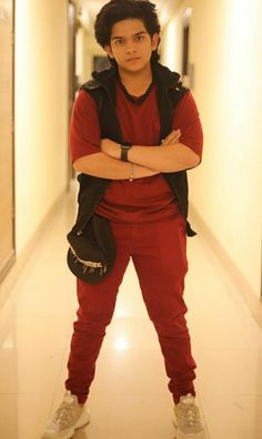 a young man standing in a hallway with his arms crossed and looking at the camera