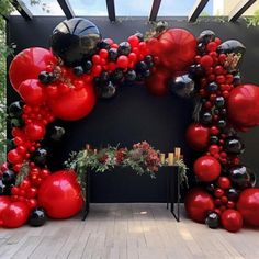 a red and black balloon arch with lots of balloons hanging from it's sides