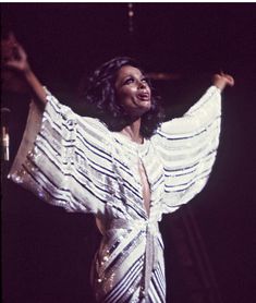 a woman in a white dress standing on stage with her arms out and hands outstretched