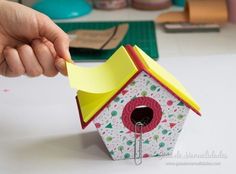 a hand holding a piece of paper over a birdhouse shaped object on a table