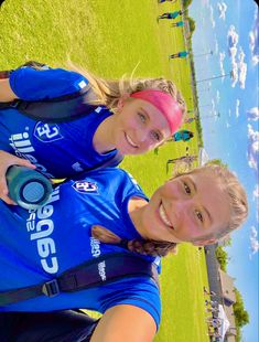 two girls in blue shirts standing next to each other on a field with grass and water