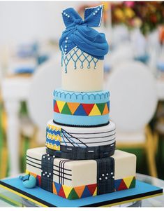 a multi - tiered cake with blue icing on top and colorful ribbons around the edges