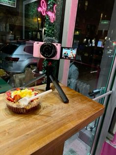 a wooden table topped with a bowl of fruit and a camera on top of it