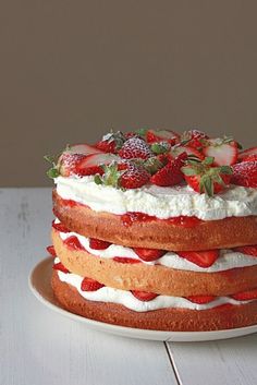 a cake with strawberries and whipped cream on top sitting on a white wooden table