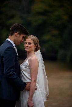 a bride and groom standing together in front of trees