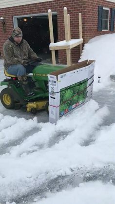 a man on a green lawn mower in front of a building with snow around it