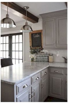 a kitchen with gray cabinets and white counter tops, two pendant lights over the island