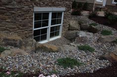 a window sitting on the side of a stone building next to flowers and rocks in front of it