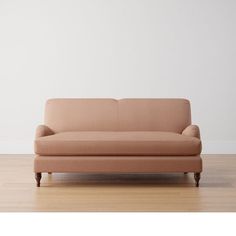 a tan couch sitting on top of a hard wood floor next to a white wall