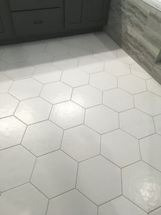 a white tiled bathroom floor with gray cabinets and counter tops, in front of a window