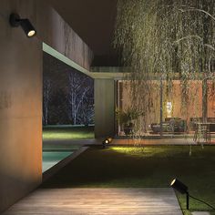 an outdoor area with a deck, table and chairs at night near a swimming pool