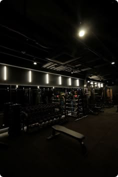 a dimly lit gym with rows of dumbbells and benches in the foreground