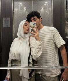 a man and woman standing in front of a mirror taking a selfie with a cell phone