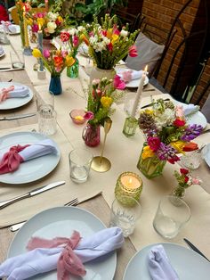 the table is set with place settings and flowers in vases, napkins, and candles