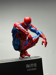 a spider man figurine sitting on top of a black box with chinese writing