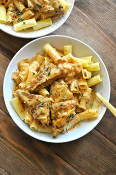 two white bowls filled with pasta and chicken on top of a wooden table next to another bowl