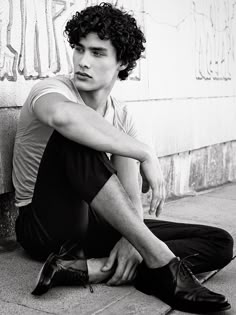 a young man sitting on the ground next to a wall with his hands on his knees