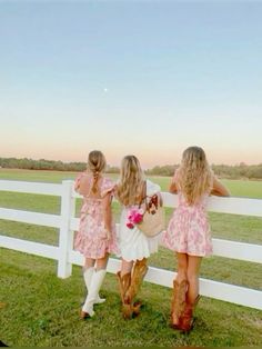 three girls in pink dresses are standing by a white fence with a horse and flowers