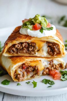 two mexican burritos on a plate with guacamole and sour cream