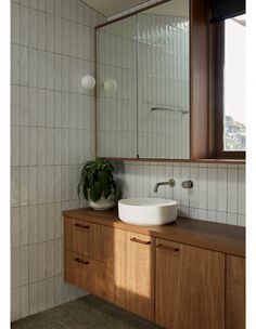 a bathroom sink sitting under a mirror next to a wooden cabinet and counter with a potted plant on it