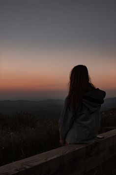 a woman sitting on top of a wooden bench looking out at the mountains in the distance