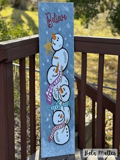 a snowman is painted on a blue sign with words believe and three snowmen