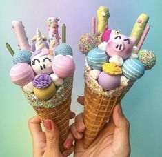 two people holding ice cream cones with marshmallows in them and decorations on top