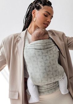 a woman holding a baby in her arms while standing next to a white wall and stairs