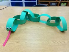 a snake made out of paper sitting on top of a wooden table next to a pink stick