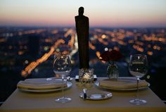 the table is set with wine glasses, plates and utensils in front of a cityscape