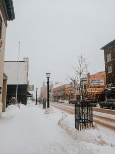 a snowy street with cars parked on the side and people walking down the sidewalk in the distance