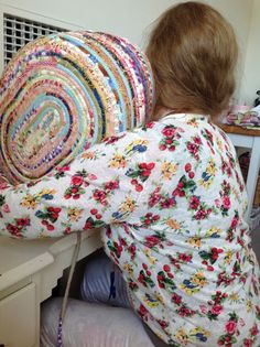 a woman sitting on top of a white chair next to a pile of quilts