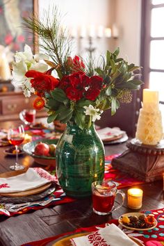 a green vase filled with red and white flowers on top of a dining room table