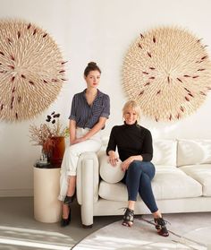 two women sitting on a white couch in front of large wall art hanging above them