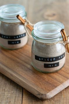 two glass jars with cinnamon sticks in them sitting on a wooden cutting board next to each other