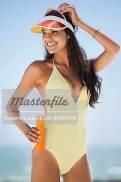 a woman in a yellow one piece swimsuit standing on the beach, holding an orange bottle