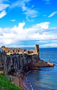 an old castle sitting on top of a cliff next to the ocean under a cloudy blue sky