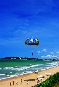 people are on the beach flying a large kite in the sky over the water and sand