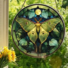 a stained glass butterfly hanging from the side of a window with flowers in front of it