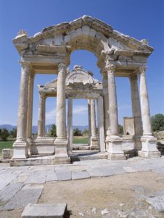 an old stone structure with pillars and arches on the ground in front of a blue sky