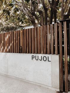 the entrance to pujol is lined with wooden slatted walls and trees