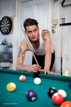 a man with tattoos leaning over a pool table