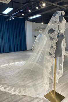 a wedding dress and veil on display in a room with blue curtained walls behind it