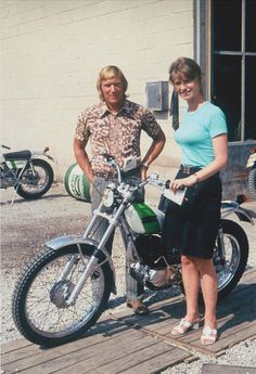 a woman standing next to a man on a motorcycle