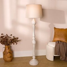 a white floor lamp sitting next to a vase with flowers on it and a brown pillow