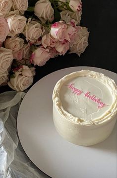 a white frosted birthday cake sitting on top of a table next to pink flowers